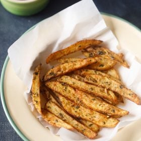 fried crispy potato wedges on parchment paper in a deep dish plate.