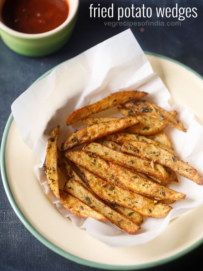 fried crispy potato wedges on parchment paper in a deep dish plate.