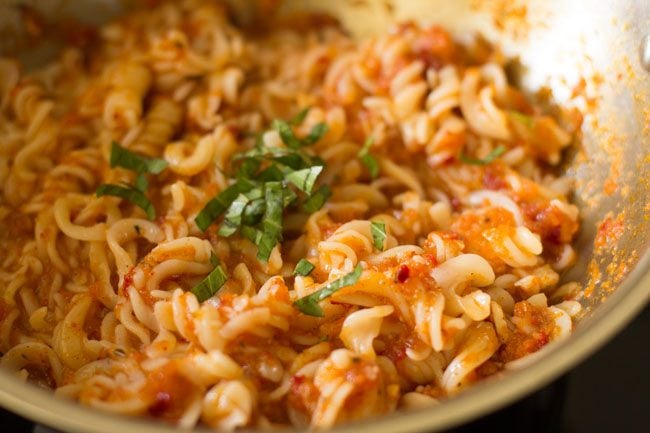 basil leaves added to pasta arrabbiata in pan