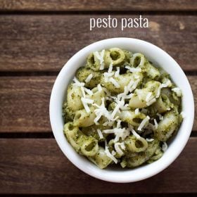 pesto pasta served in a white bowl topped with some grated parmesan on a dark brown wooden tray