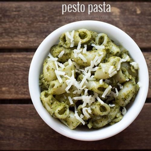 pesto pasta served in a white bowl topped with some grated parmesan on a dark brown wooden tray