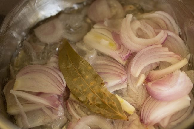 thinly sliced onions and bay leaf added to the hot coconut oil. 