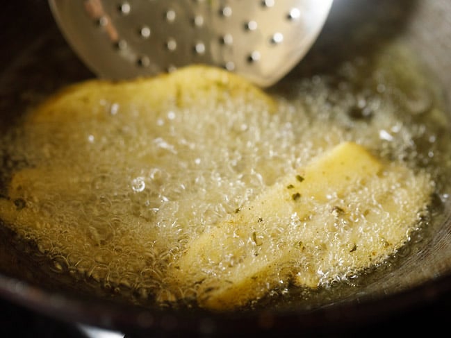 golden potato wedges being turned over with a slotted spoon