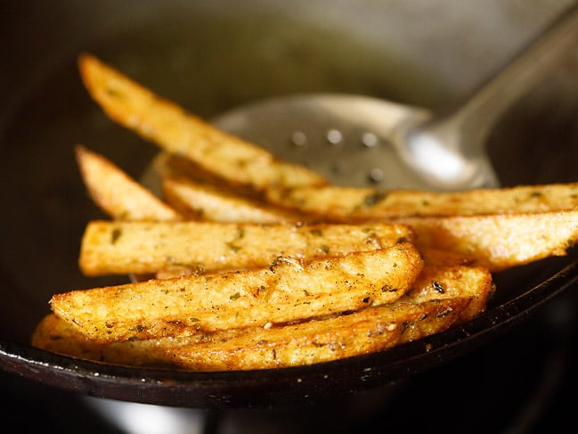fried potato wedges removed using a slotted spoon