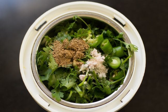 coriander leaves, mint leaves, chopped green chilies, garlic clove, black salt and dried mango powder added to a grinder jar. 