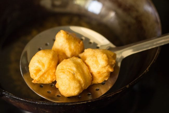 removing fried pakodas from the hot oil using a slotted spoon. 