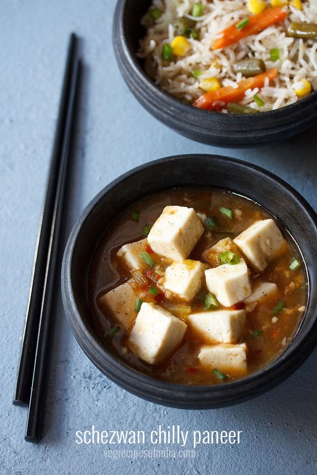 schezwan paneer served in a back bowl with a side of fried rice