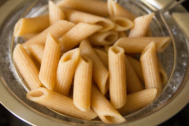 cooked penne pasta being removed with a strainer spoon. 