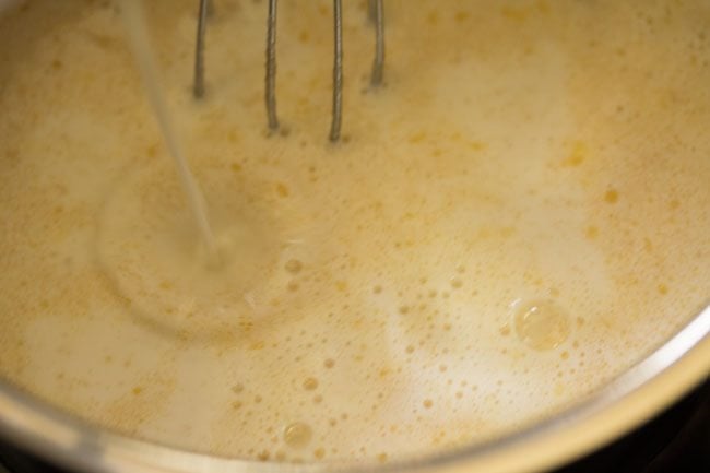 adding chilled milk to the pan for making white sauce pasta recipe. 