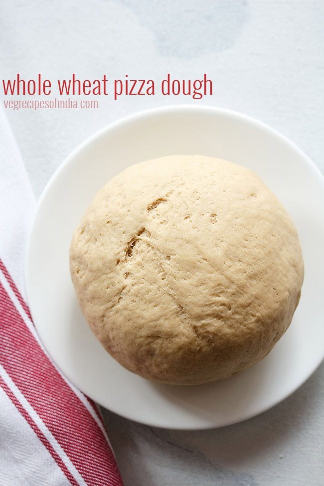 whole wheat pizza dough on a white plate with a red and white striped kitchen towel.