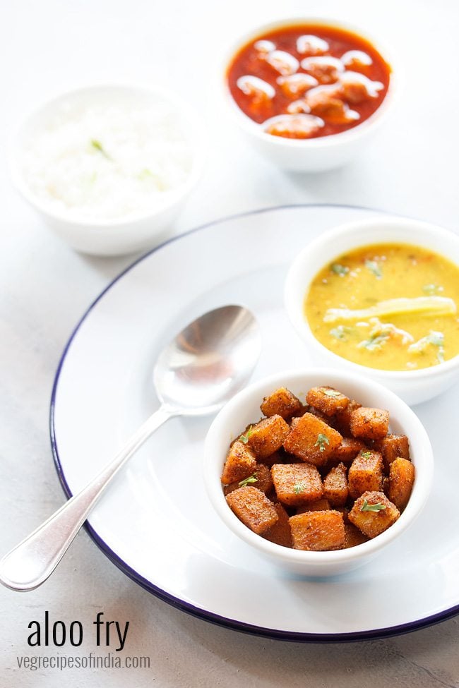 potato fry served in a bowl placed on a white plate with lentil curry in another bowl