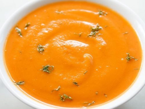 white bowl filled with carrot ginger soup and garnished with fresh green herbs.