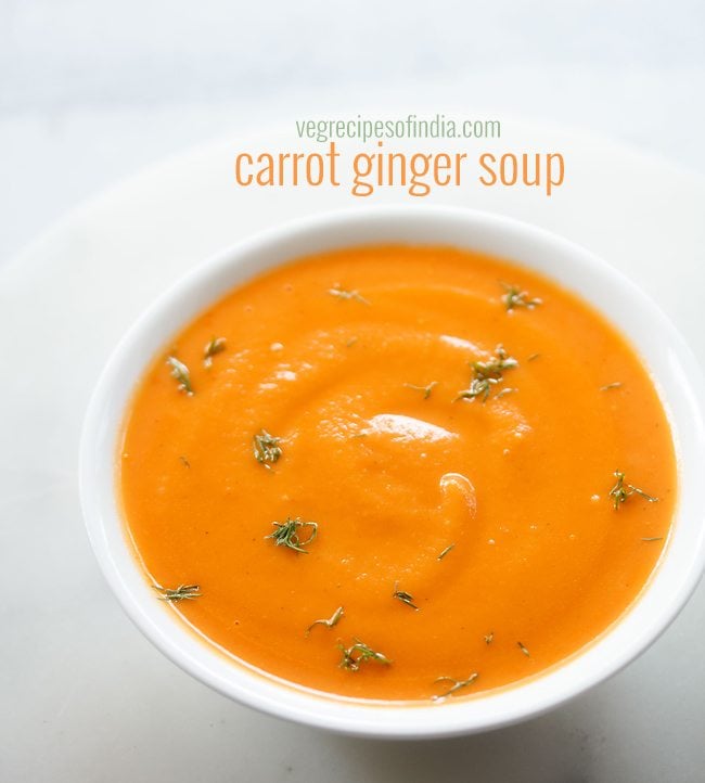 white bowl filled with carrot ginger soup and garnished with fresh green herbs. 