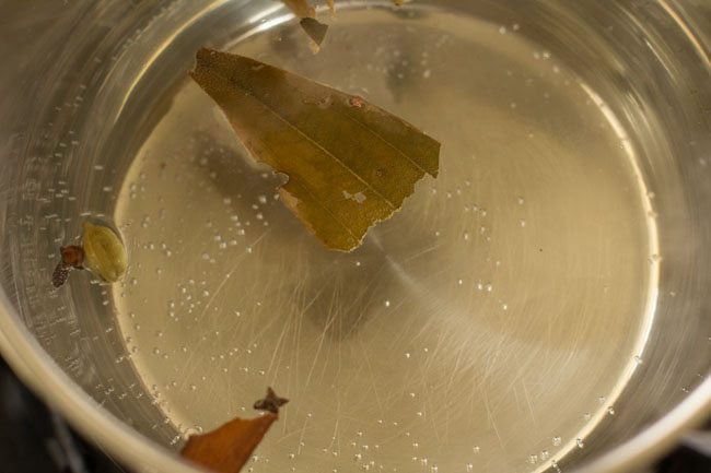 boiling water in a pan with salt, bay leaf, cloves, green cardamoms, cinnamon and mace. 