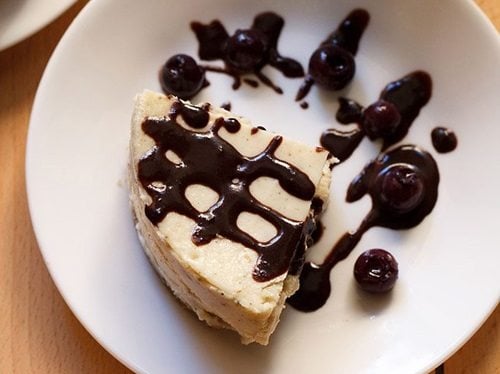 eggless cheesecake slice topped with blueberry sauce on a white plate.