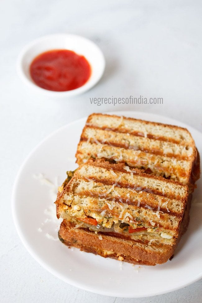 paneer sandwich with cheese served on a white plate with a bowl of sauce kept on the top left side and text layover. 