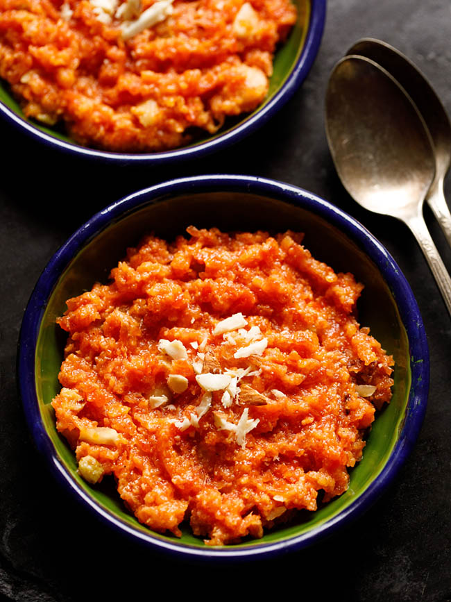 instant pot gajar halwa served in a two dark green small plates with two brass spoons at the sides