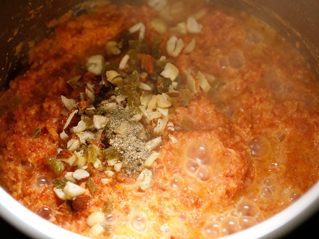 nuts, raisins and cardamom powder added to simmering carrot halwa mixture in instant pot