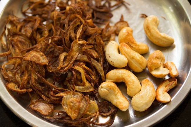 fried cashews kept with  fried onions on a steel plate. 