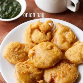 onion bajji served on a white plate with a bowl of green chutney and a cup of tea kept in the background and text layover.