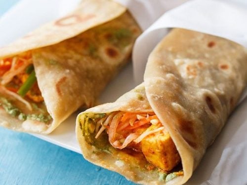 two paneer rolls wrapped in butter paper and placed on a square white plate.