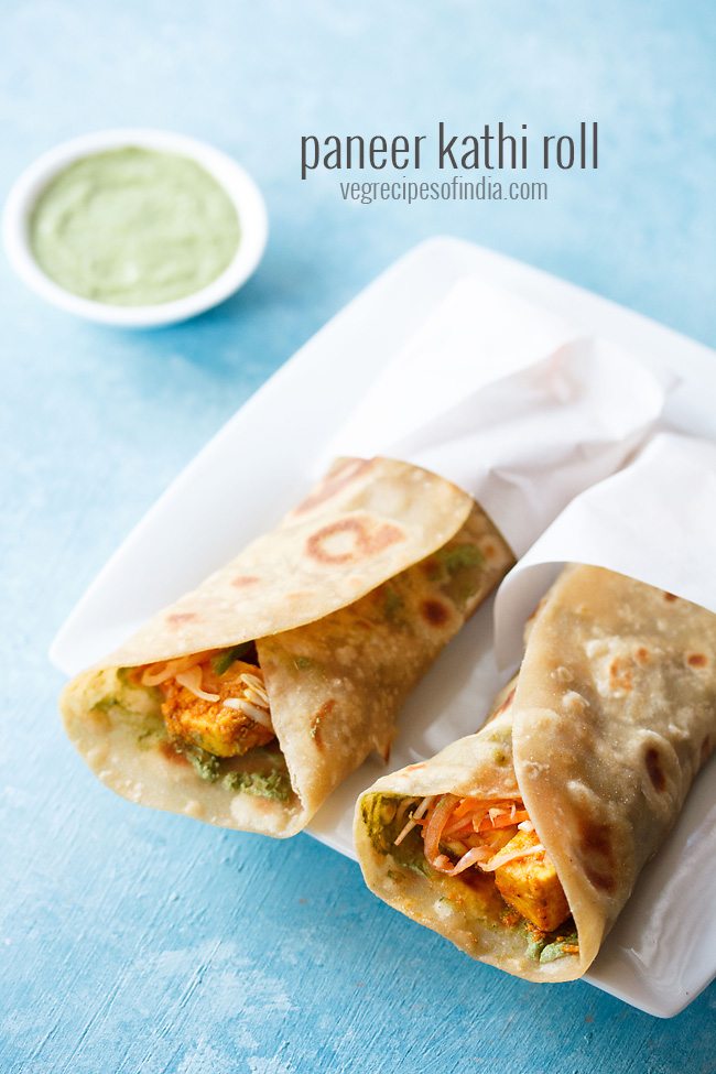 two paneer rolls wrapped in butter paper and placed on a square white plate. 