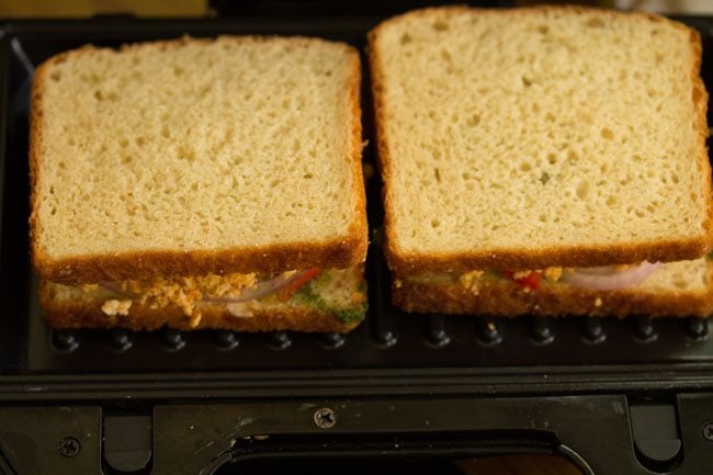 prepared paneer sandwiches placed on a preheated sandwich maker. 