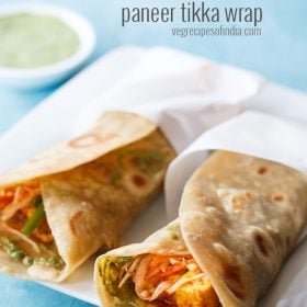 two paneer rolls wrapped in butter paper and placed on a square white plate.