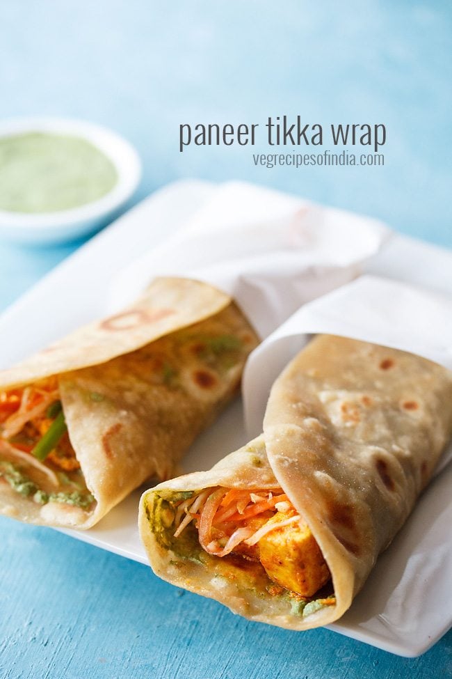 two paneer rolls wrapped in butter paper and placed on a square white plate.