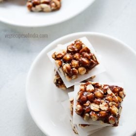 top shot of peanut chikki squares placed on parchment squares in layers on a white plate