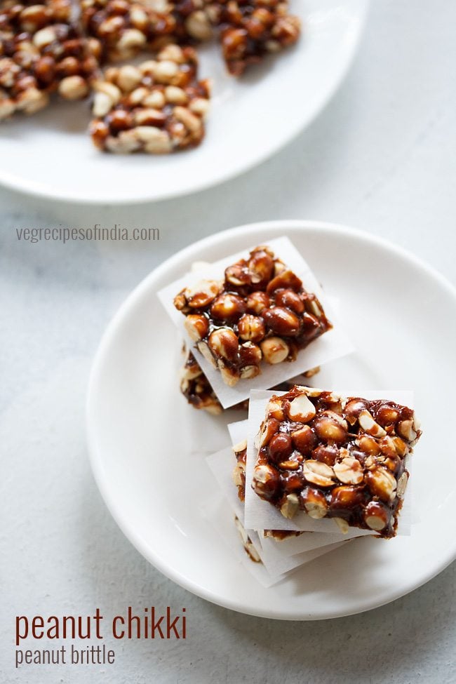 top shot of peanut chikki squares placed on parchment squares in layers on a white plate