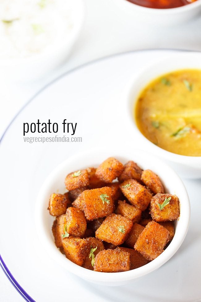 potato fry served in a bowl placed on a white plate with lentil curry in another bowl