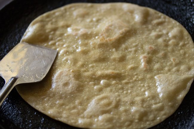 pressing the edges of the roti down with a metal spatula.