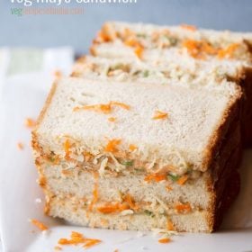 mayonnaise sandwich topped with grated carrots and cheese on a square white plate