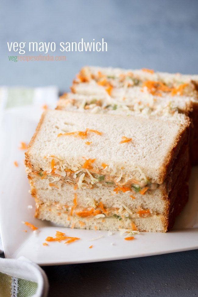 mayonnaise sandwich topped with grated carrots and cheese on a square white plate