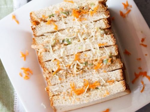 mayonnaise sandwich topped with grated carrots and cheese on a square white plate
