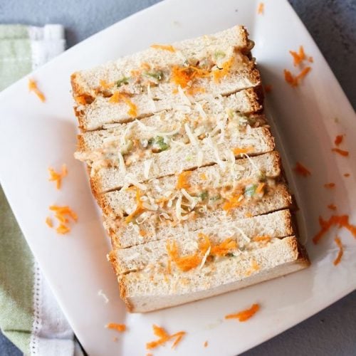 mayonnaise sandwich topped with grated carrots and cheese on a square white plate