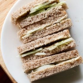 close up shot of stacked cucumber sandwiches with the visible layers of cucumber and bread placed on a white plate