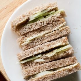 close up shot of stacked cucumber sandwiches with the visible layers of cucumber and bread placed on a white plate