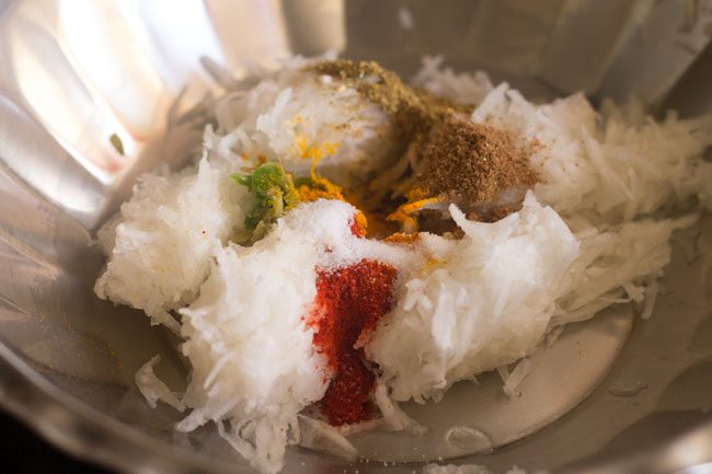 spice powders, ginger-green chili paste and salt added to grated radish in a steel bowl. 