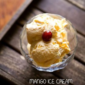 mango ice cream scoops in an ice cream bowl topped with a red cherry on a wooden tray