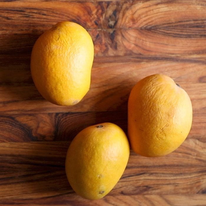 three mangoes placed on a wooden chopping board