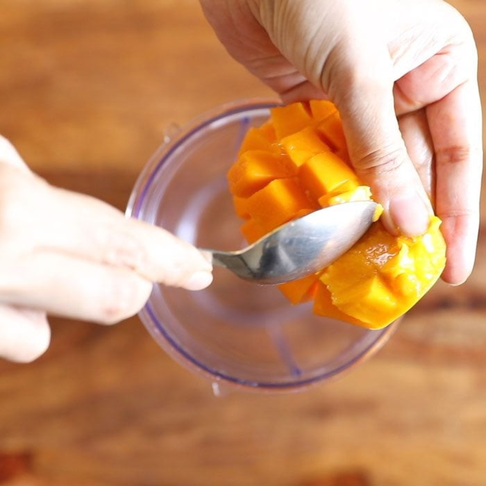 mango cubes from a mango slice being added by a spoon to a blender