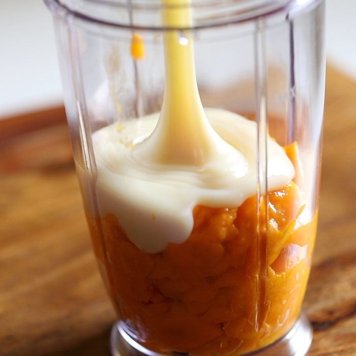 condensed milk being poured in the mangoes inside the blender