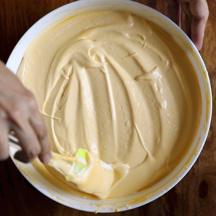 mango ice cream mixture being levelled with a spatula in a white bowl