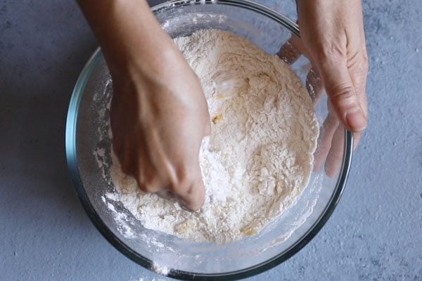 flour and ghee being mixed with fingers in bowl. 