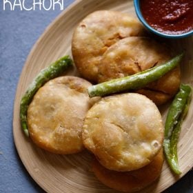 four kachori in an oval tray with few fried green chillies on top.