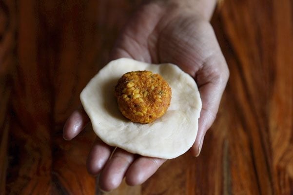 flattened dough with lentil ball on a palm. 