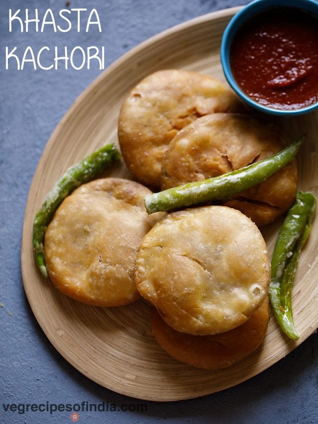 four kachori in an oval tray with few fried green chillies on top.