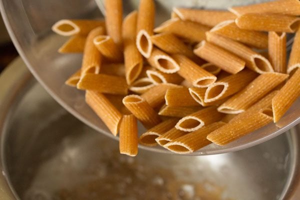 adding penne pasta to boiling water. 